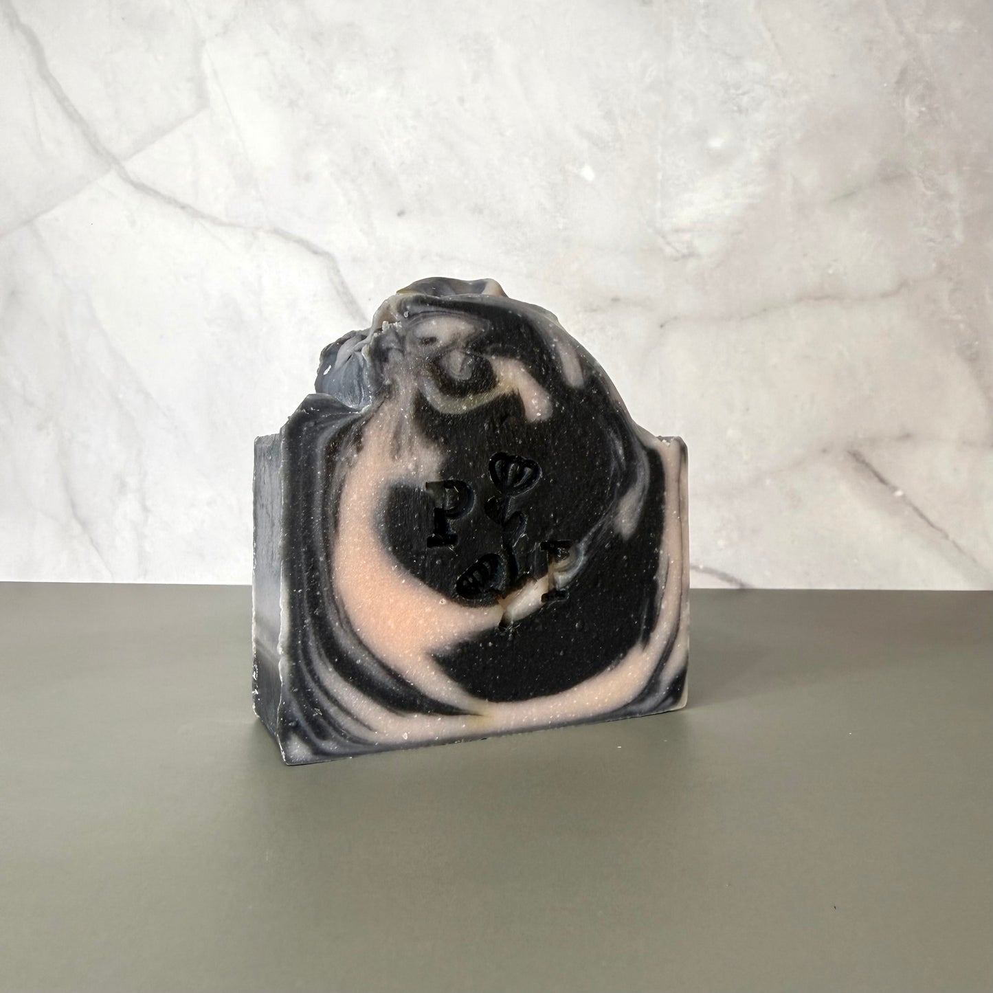 Handcrafted soap bar named Ebony Rose, deep charcoal-toned bar with subtle botanical texture, fragrance-free