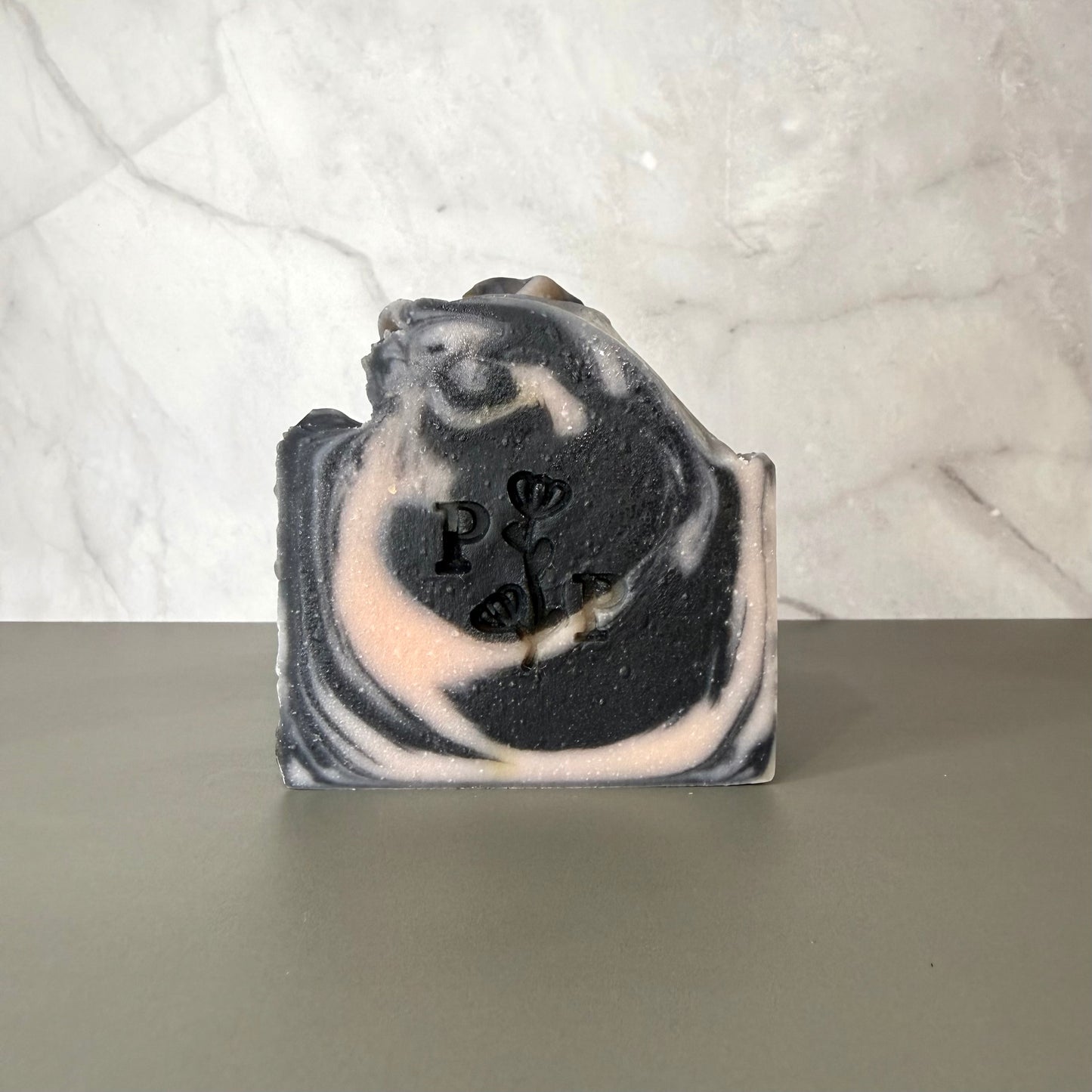 Handcrafted soap bar named Ebony Rose, deep charcoal-toned bar with subtle botanical texture, fragrance-free