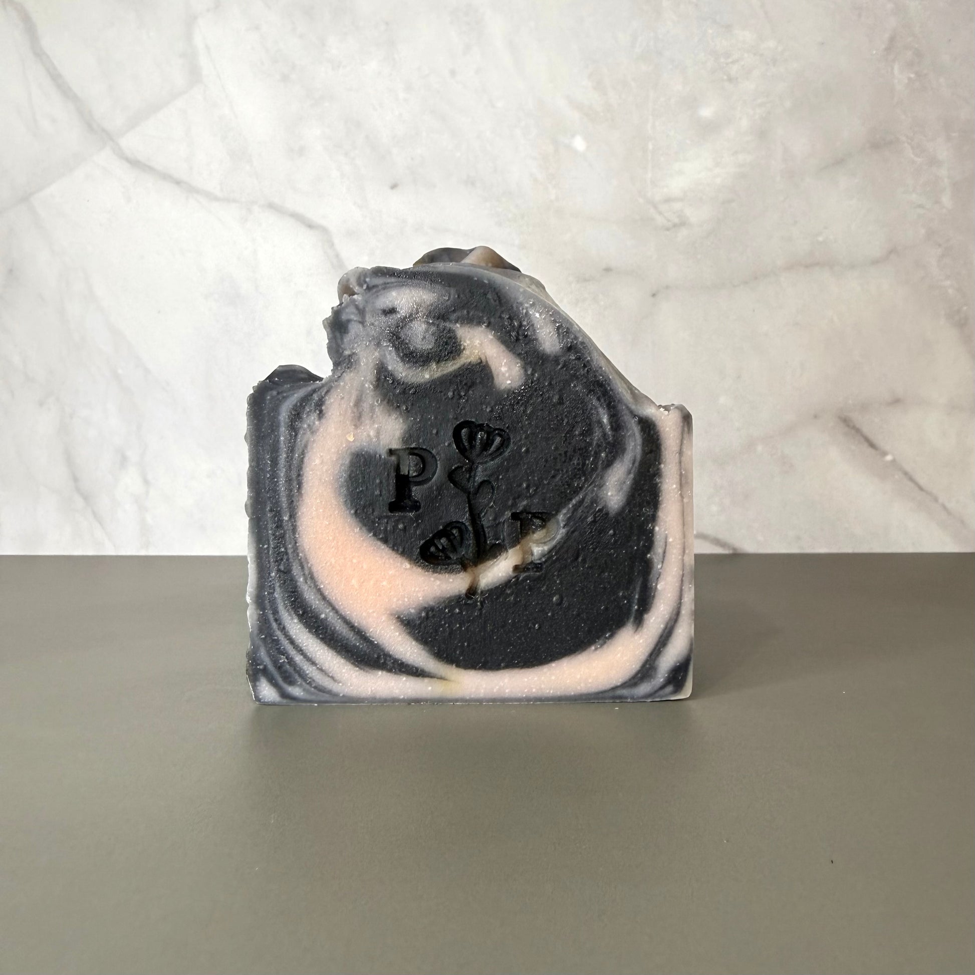 Handcrafted soap bar named Ebony Rose, deep charcoal-toned bar with subtle botanical texture, fragrance-free
