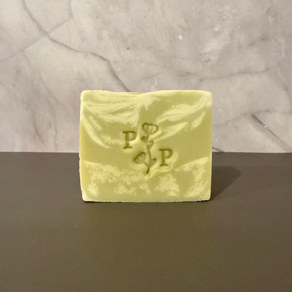 Green and cream soap bar with a logo on a gray surface and light gray background